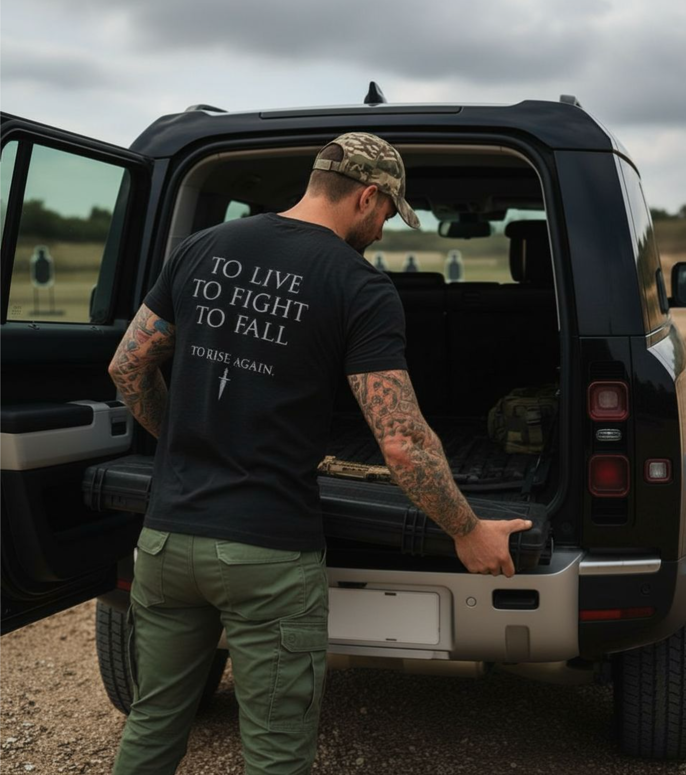 Man with tattoos and a black t-shirt with text standing next to an open SUV.