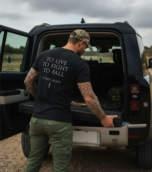 Man with tattoos and a black t-shirt with text standing next to an open SUV.