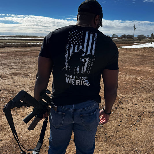 A person standing outdoors wearing a black t-shirt with a graphic design of an American flag and text on the back.