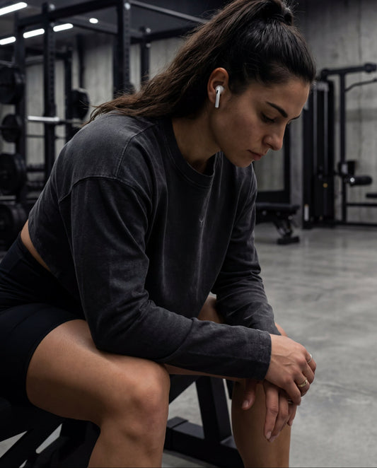 Woman sitting on a bench in a gym wearing wireless earbuds.