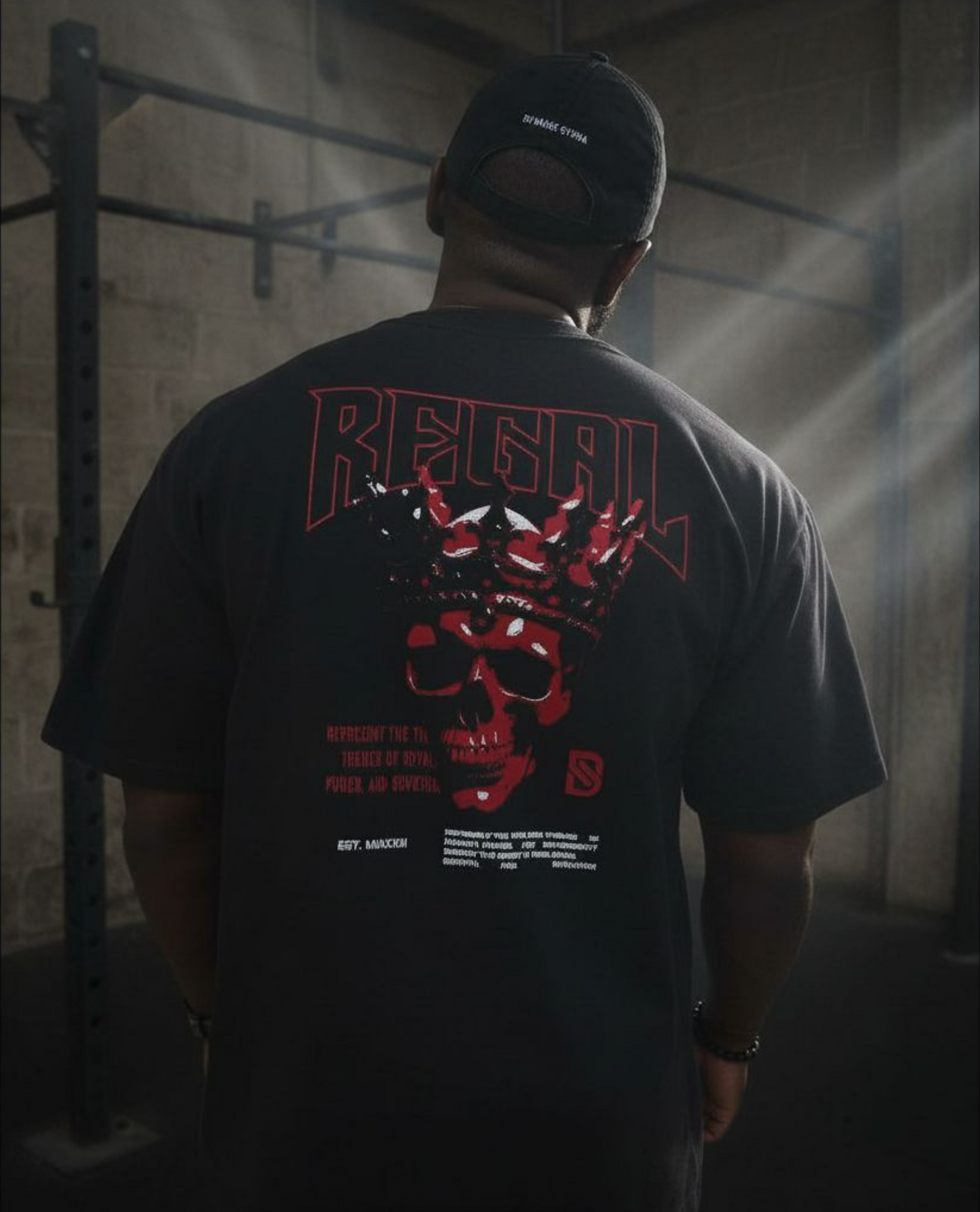 Person wearing a black t-shirt with red and white graphics and text, standing in a dimly lit room.