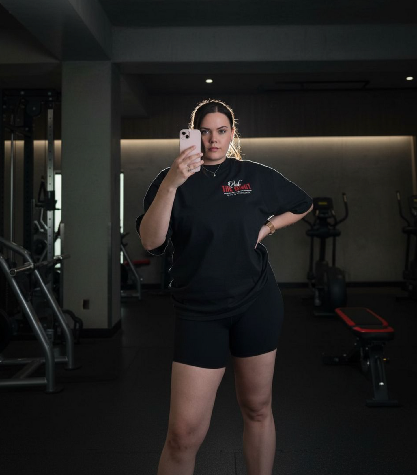 Person taking a mirror selfie in a gym wearing a black outfit with a logo.