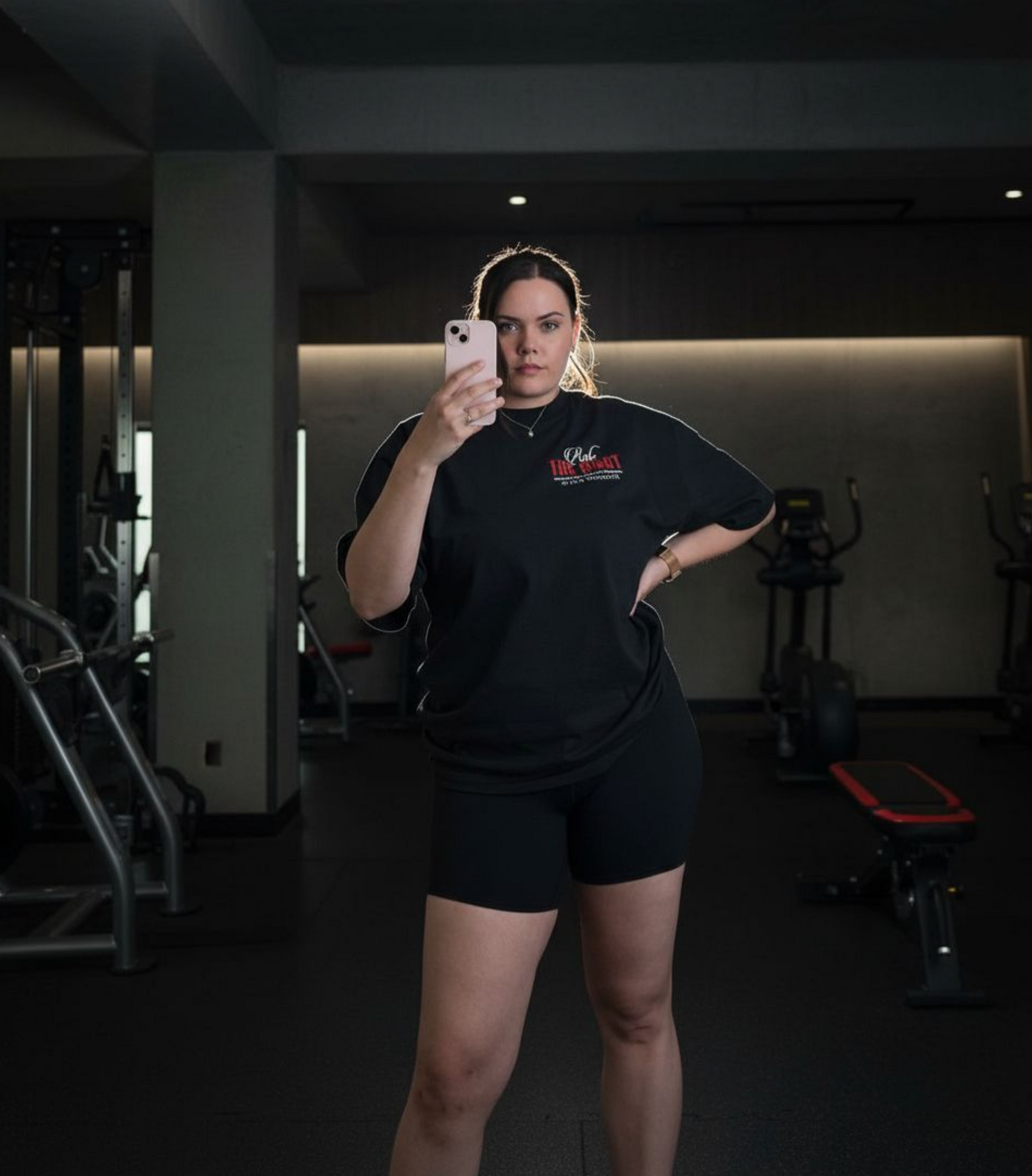 Person taking a mirror selfie in a gym wearing a black outfit with a logo.