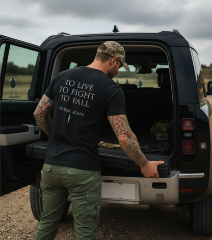Man with tattoos and a black t-shirt with text standing next to an open SUV.